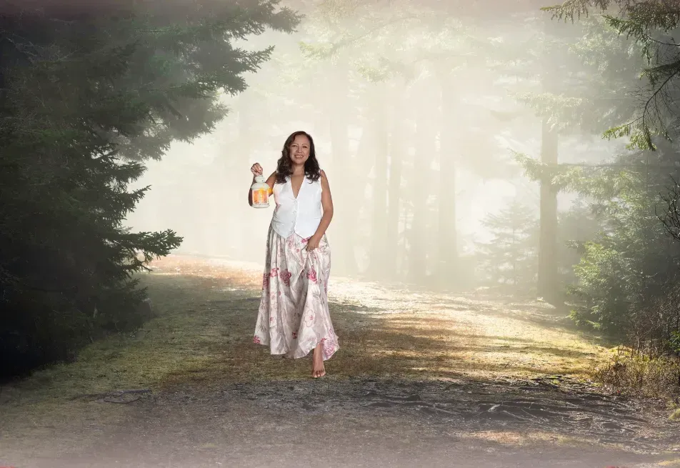 Mujer caminando por un sendero forestal brumoso, llevando una linterna.