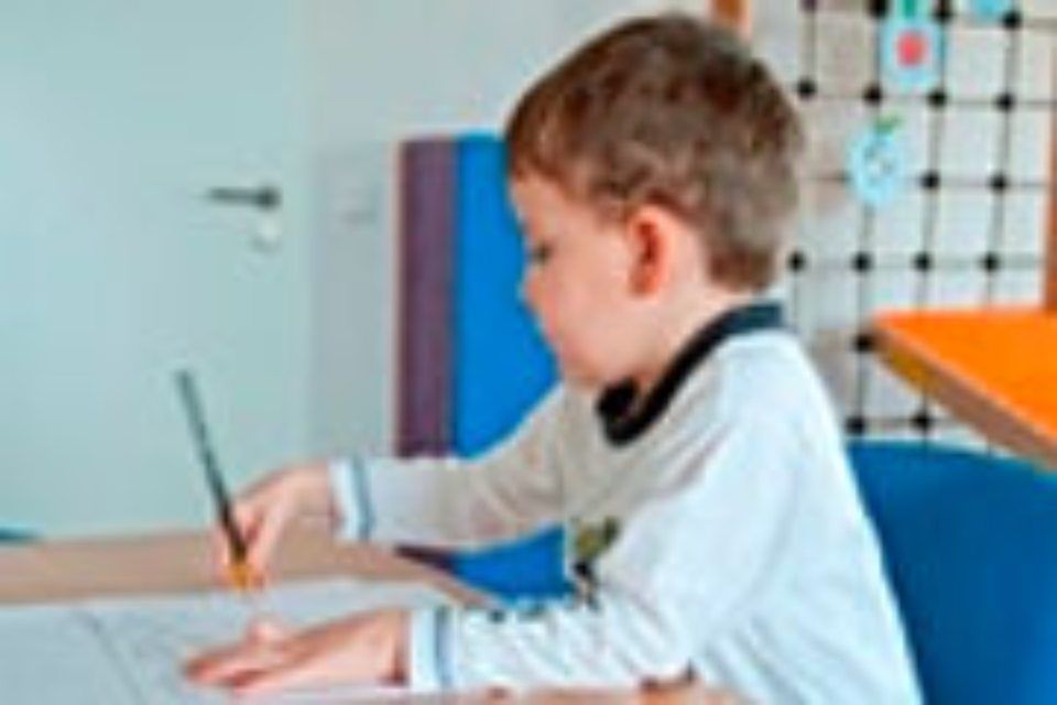 Praxis für Ergotherapie und Logopädie Brückner - Kleiner Junge am Schreibtisch malt oder schreibt mit einem Stift