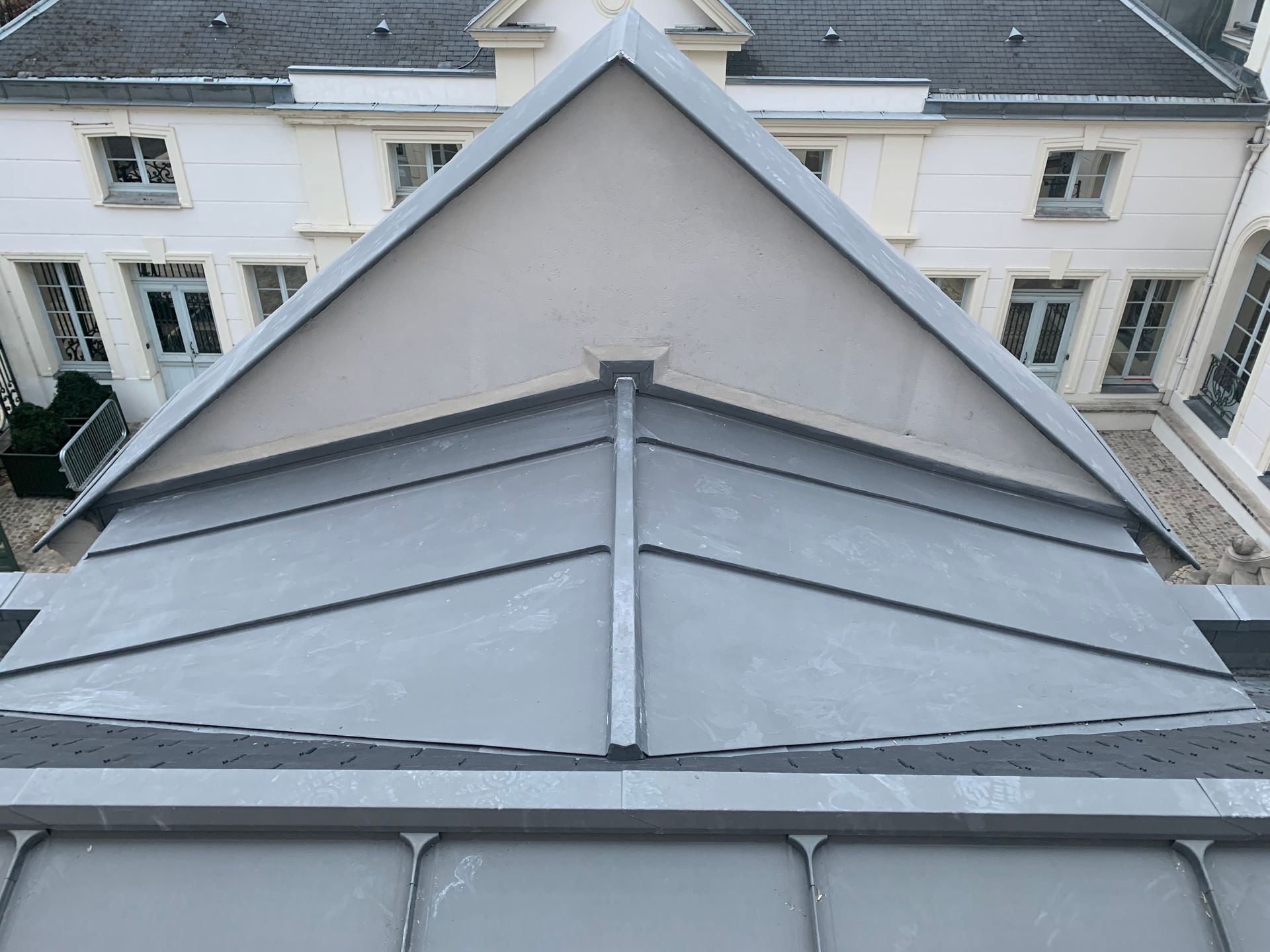 Toiture métallique grise à pignon triangulaire sur un bâtiment blanc avec des fenêtres.