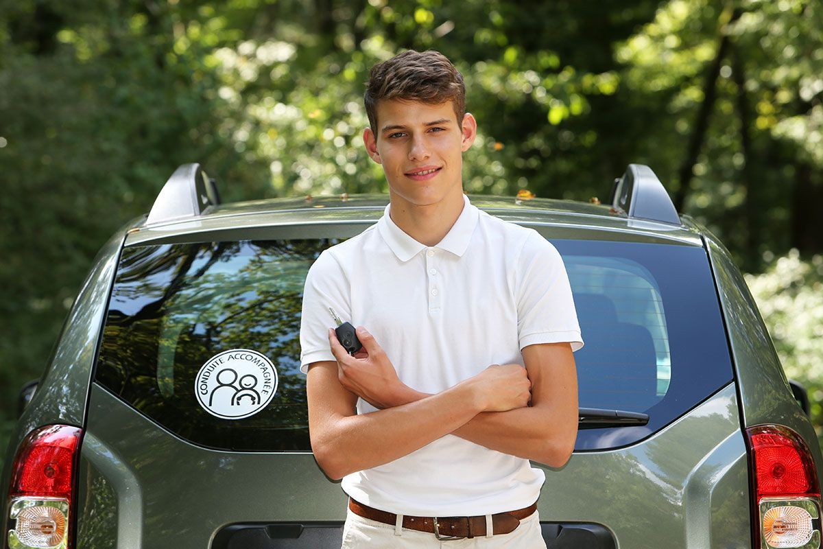 Jeune homme devant une voiture avec un sticker conduite accompagnée