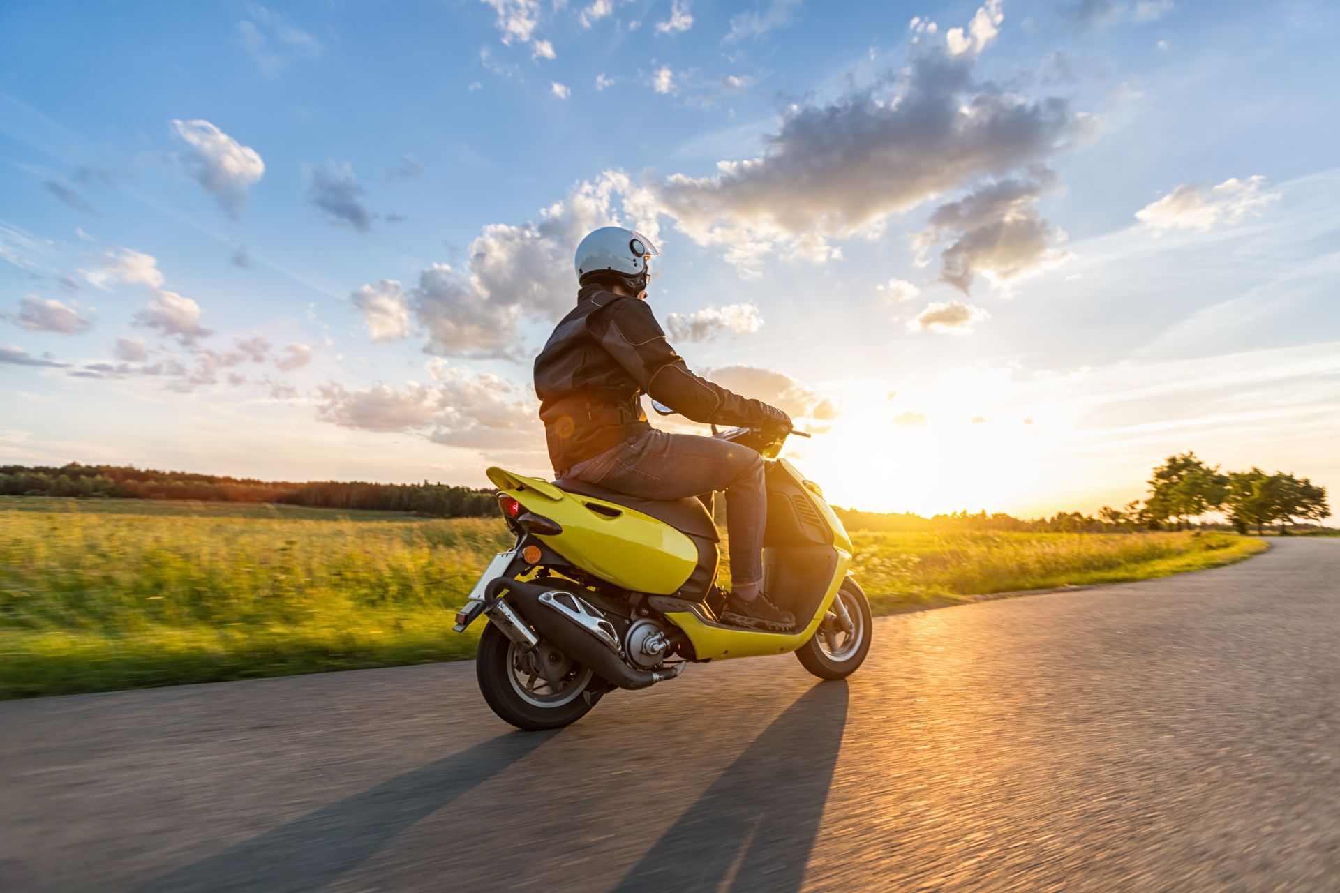 Homme conduisant un scooter sur une route de campagne au soleil couchant