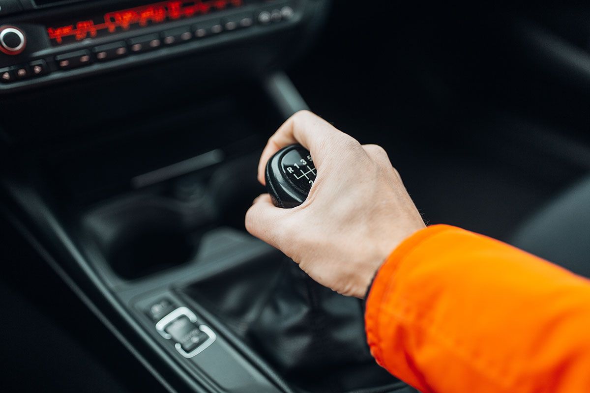 Focus sur la main d'un homme avec un pull orange qui passe les vitesses sur une boîte manuelle