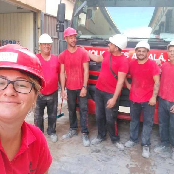 Una mujer que lleva un casco de seguridad se encuentra frente a un grupo de hombres con camisas rojas.