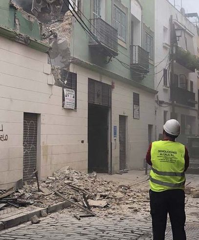 Un hombre con un chaleco amarillo está parado frente a un edificio que se ha derrumbado.