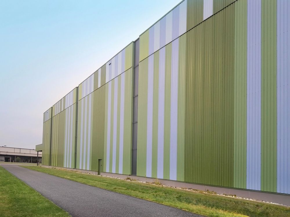 Ein langes, grün-weißes Industriegebäude neben einem gepflasterten Weg unter blauem Himmel
