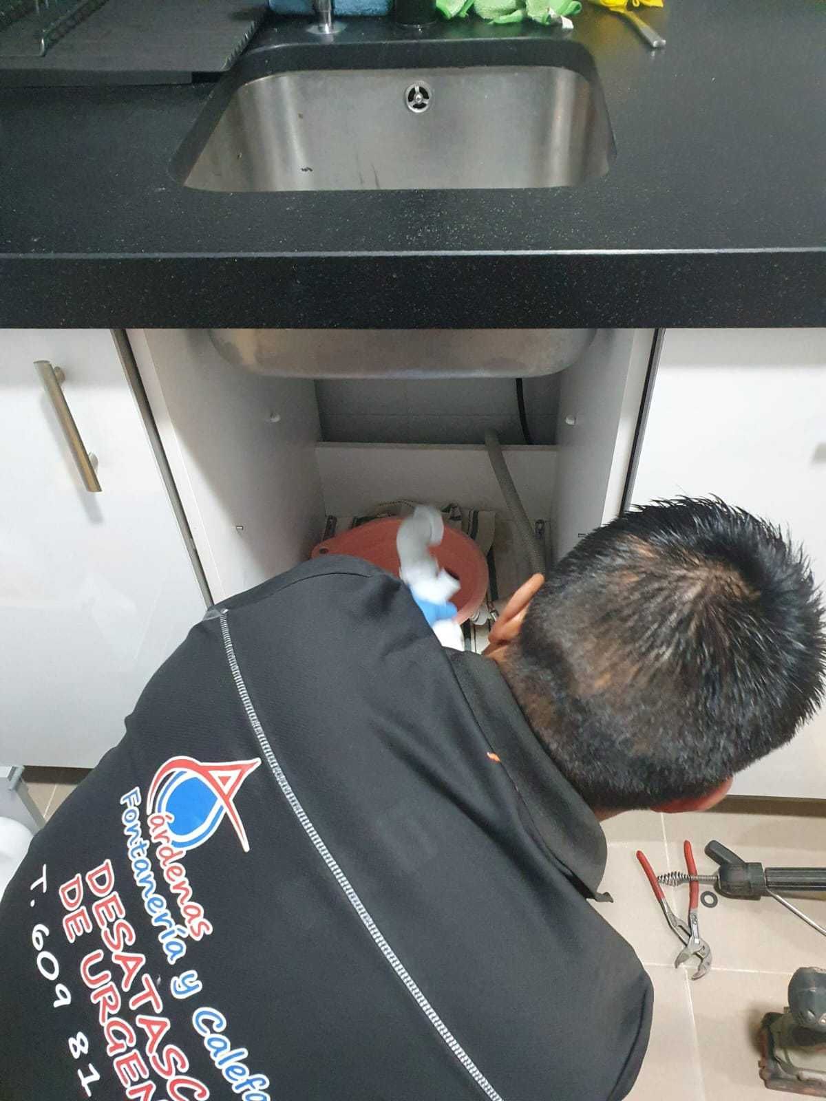 Un fontanero trabajando debajo del fregadero de la cocina, con herramientas cerca.