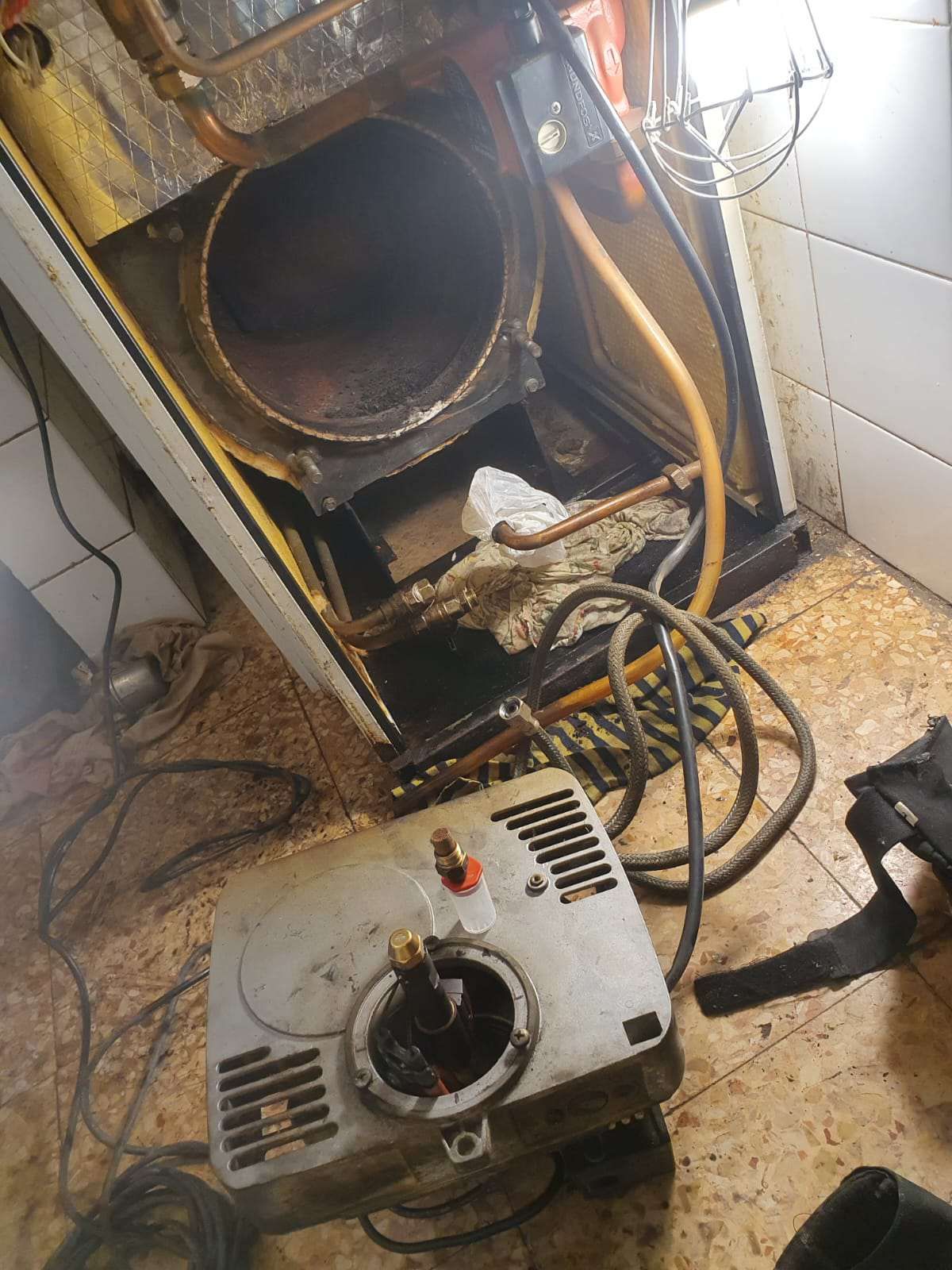 Componentes del calentador de agua a gas en el suelo, desmontados. Vista interior del tanque abierto. Cables y tuberías de gas visibles.