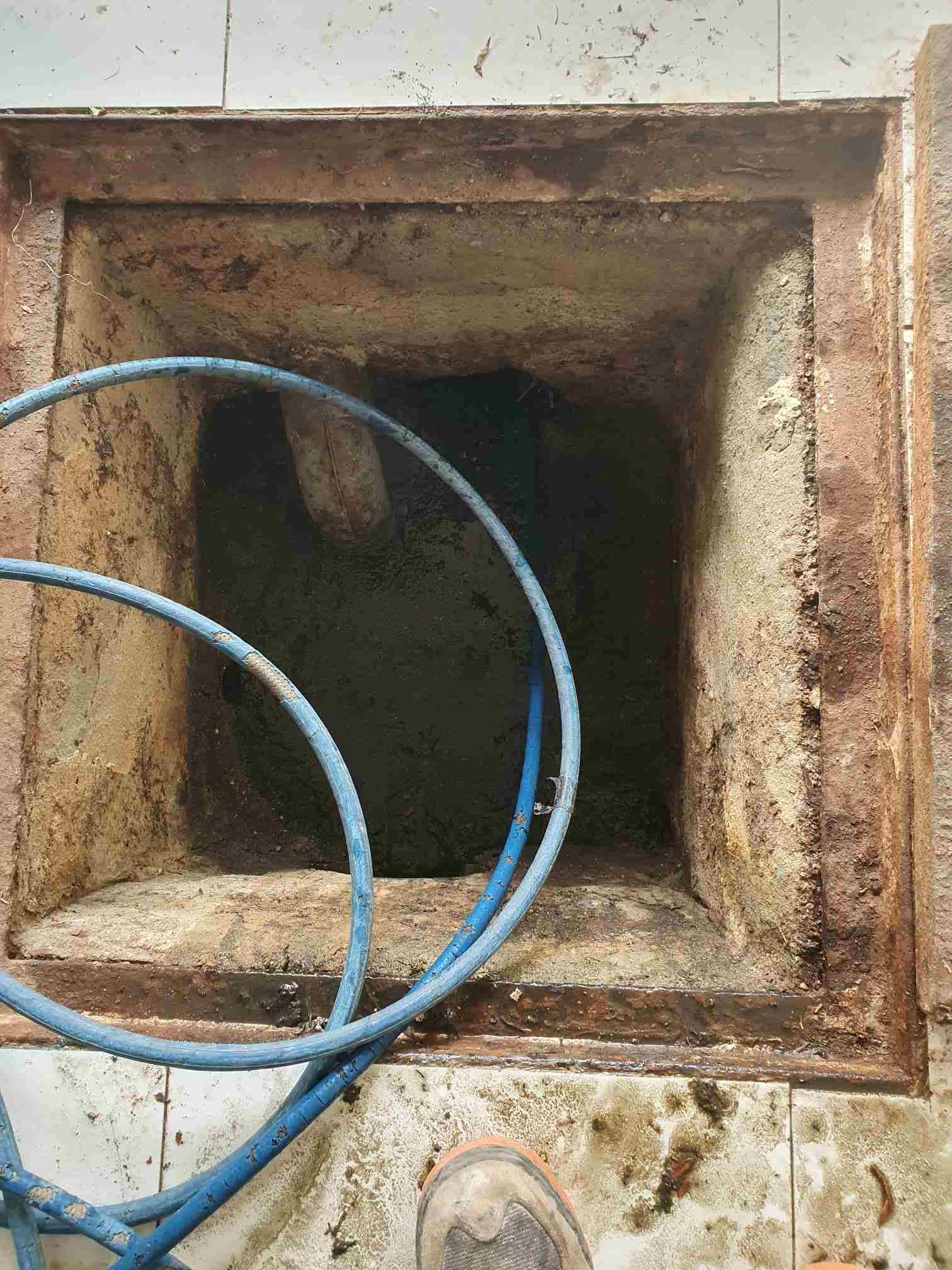 Punto de acceso abierto y cuadrado en el suelo de baldosas, con una manguera azul en su interior.