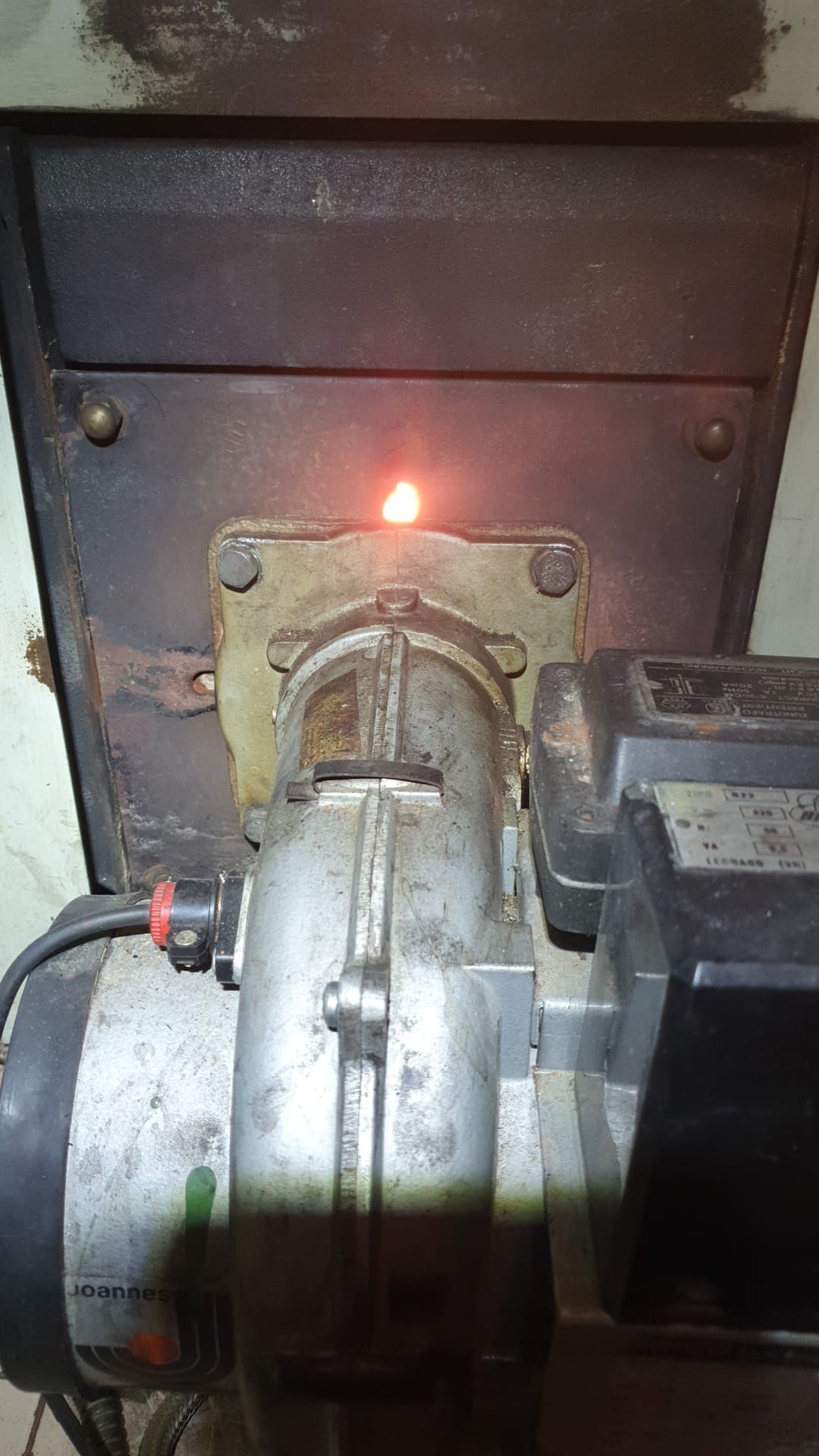 Quemador de aceite con una pequeña llama visible, montado dentro de un horno.