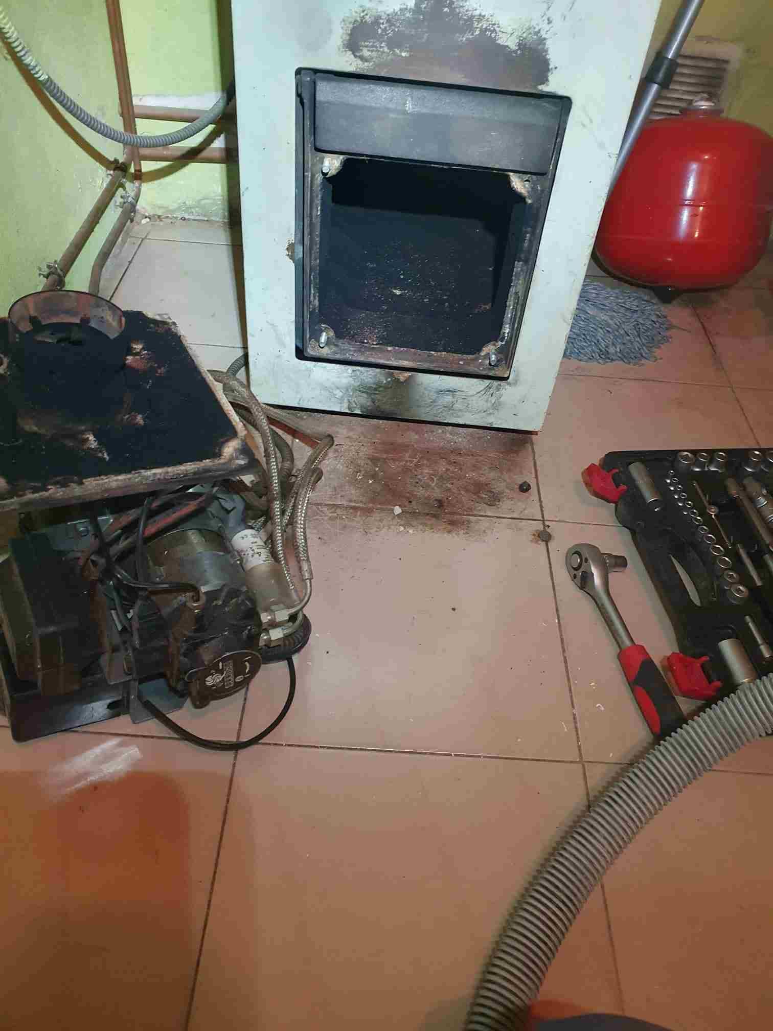 Horno con quemador independiente, herramientas y un tanque de expansión rojo sobre suelo de baldosas.