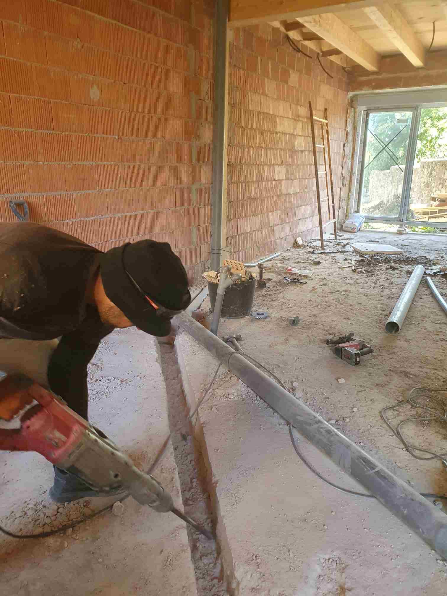 Obrero de la construcción utilizando una sierra eléctrica para cortar el suelo de hormigón junto a una pared de ladrillo.