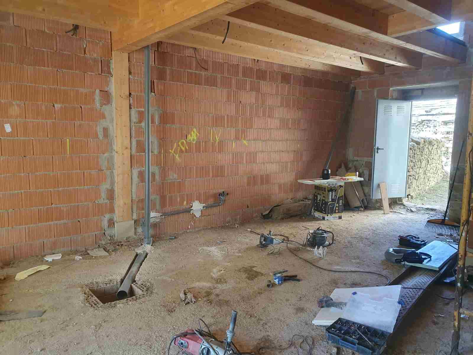 Escenario interior de una obra en construcción con paredes de ladrillo visto, tuberías y herramientas.