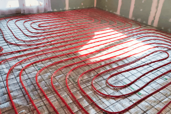 Tubos rojos de calefacción radiante por suelo dispuestos en bucles sobre una rejilla metálica, listos para su instalación.