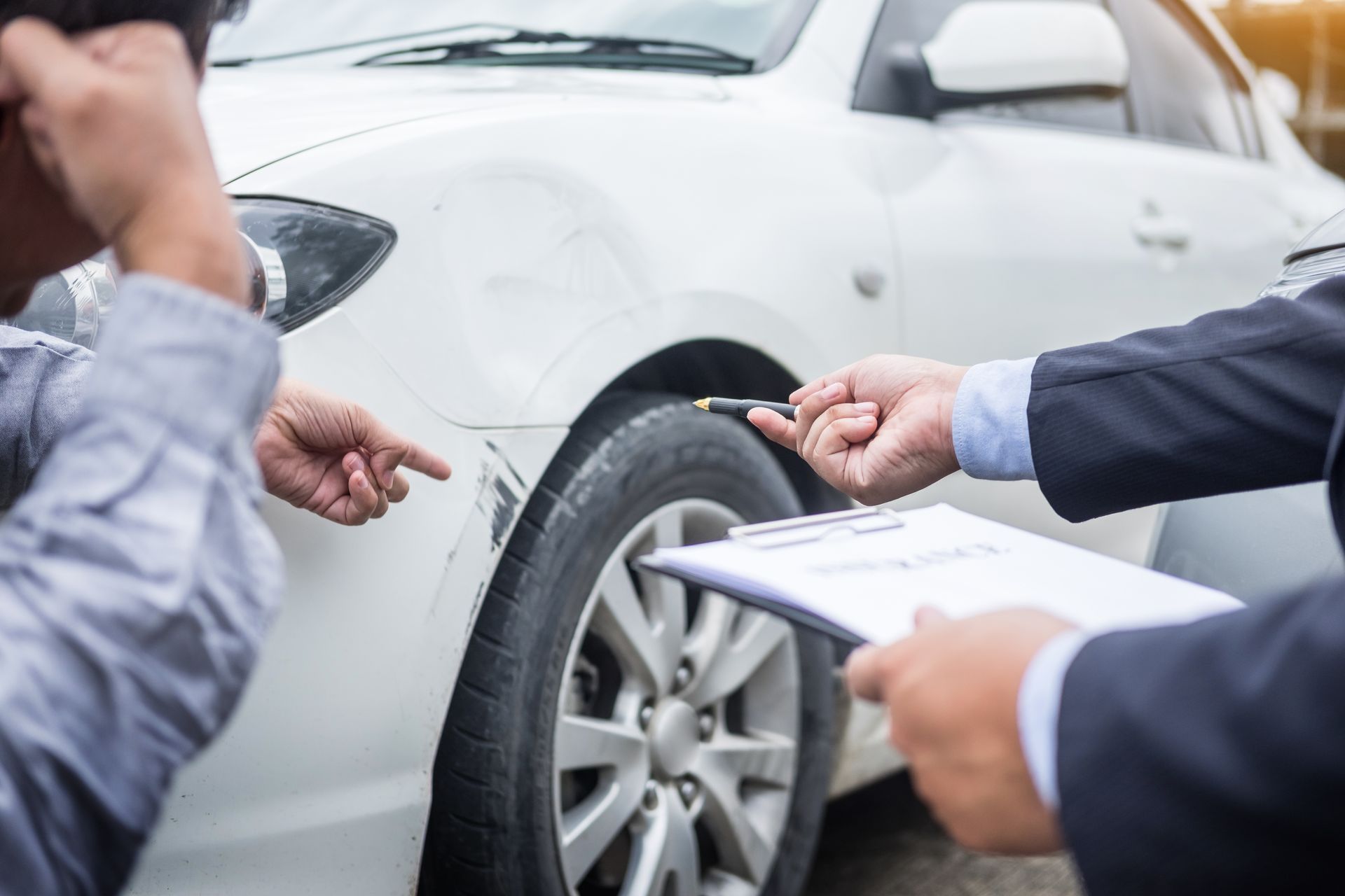 zwei Menschen besprechen einen Lackschaden eines weißen Autos.