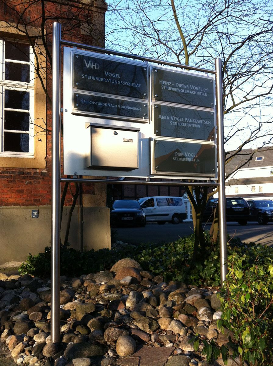 Ein Schild an einem Mast vor einem Gebäude mit der Aufschrift „vhs“