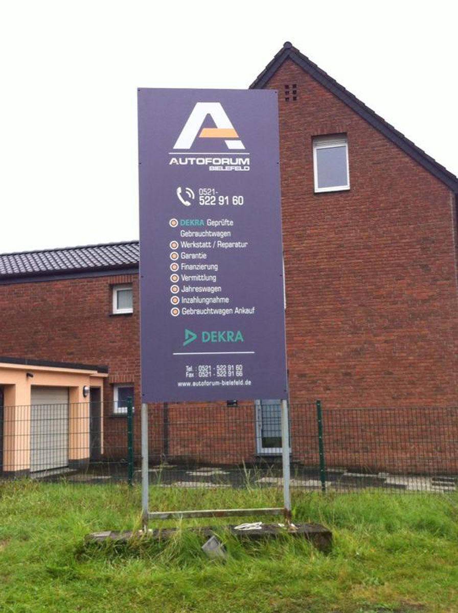 Vor einem Backsteingebäude steht ein großes violettes Schild.