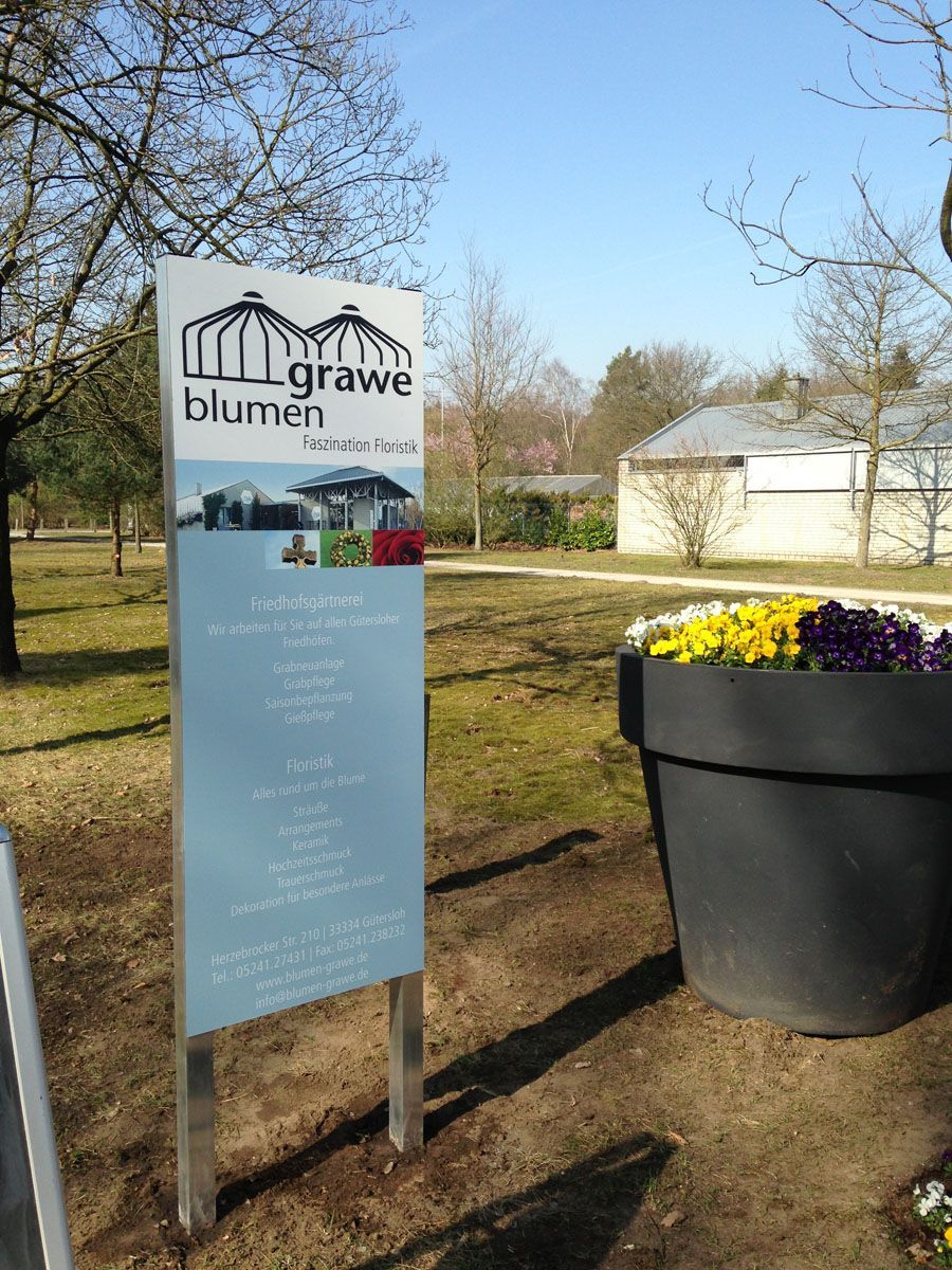 Neben einem Blumentopf steht ein Schild mit der Aufschrift „Blumen“.