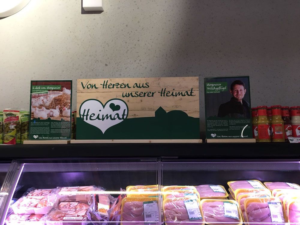 A butcher 's display case with meats and a sign that says ' von herzen aus unserer heimat '