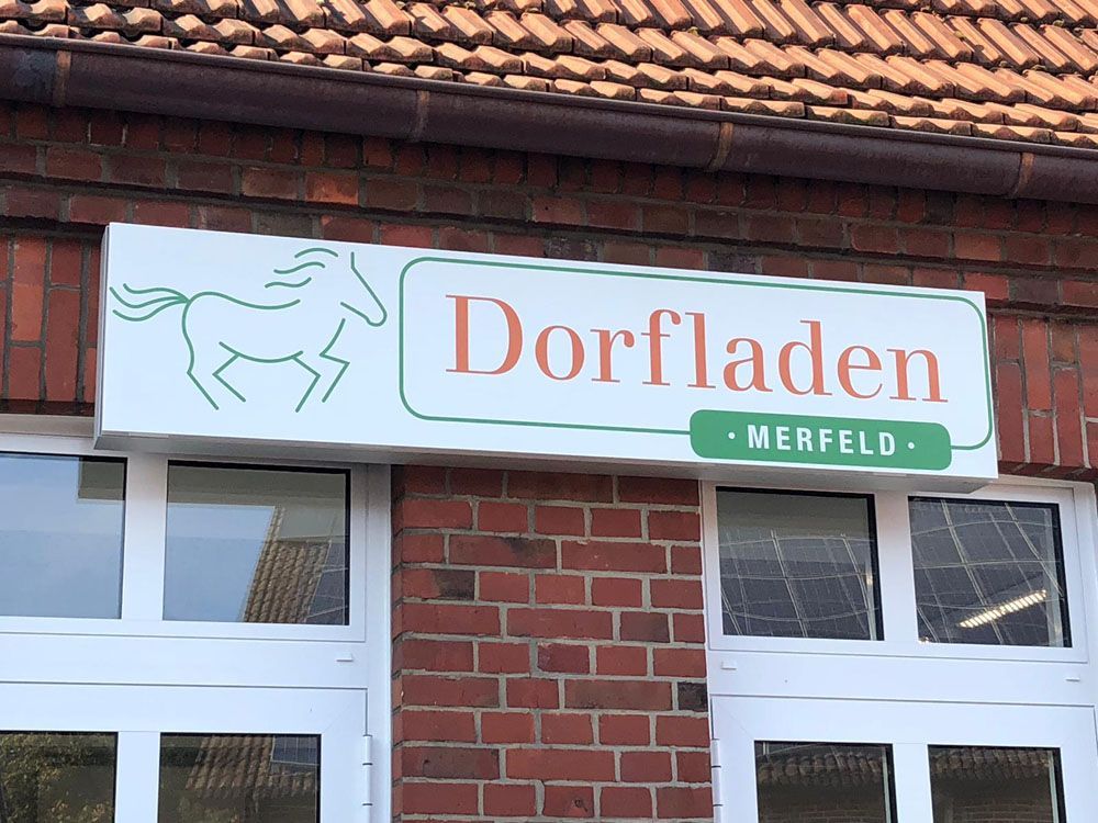 Ein Schild an einem Backsteingebäude sagt Dorfladen Merfeld