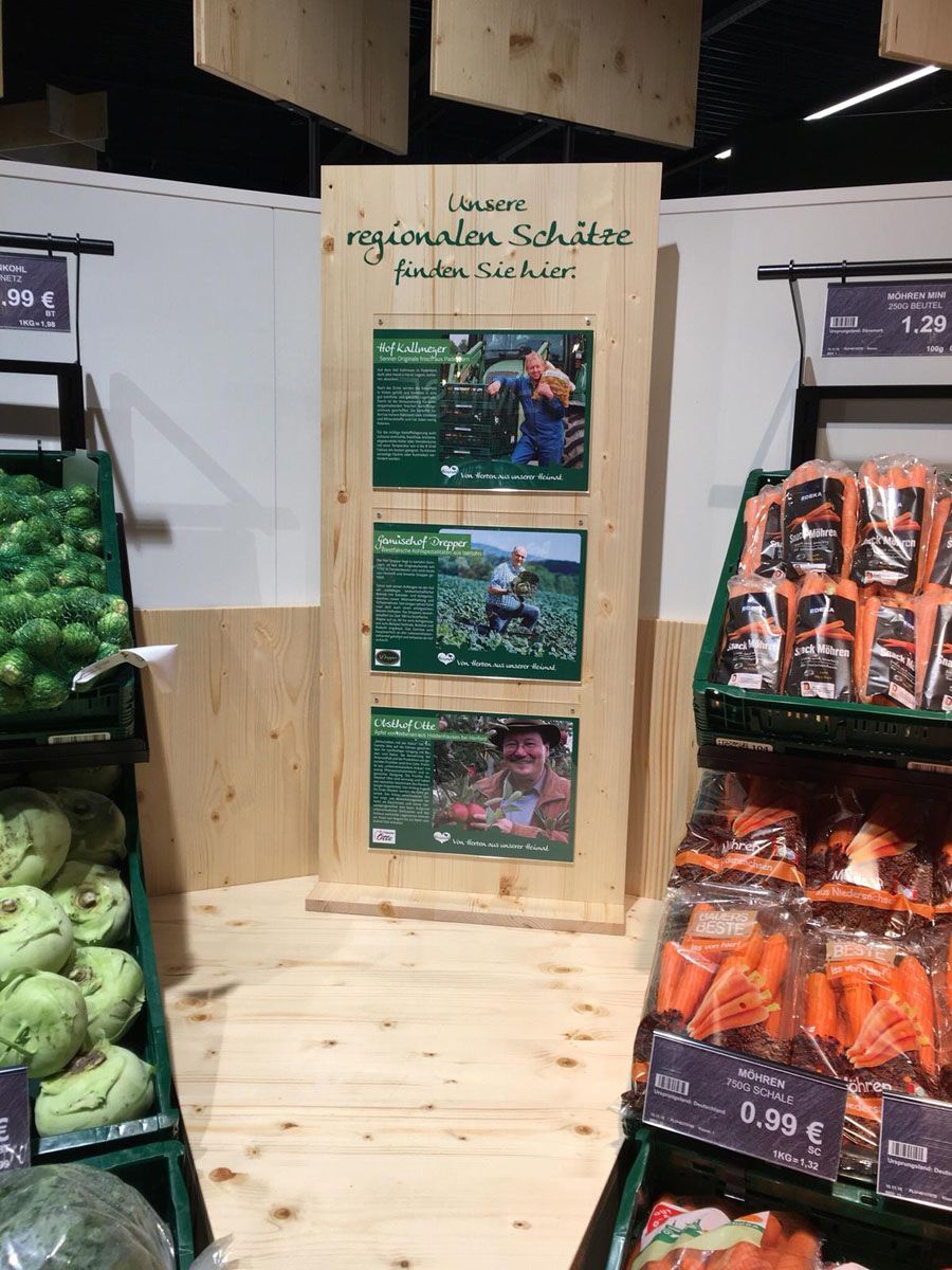 Eine Gemüseauslage in einem Lebensmittelgeschäft mit einem Holzschild an der Wand.