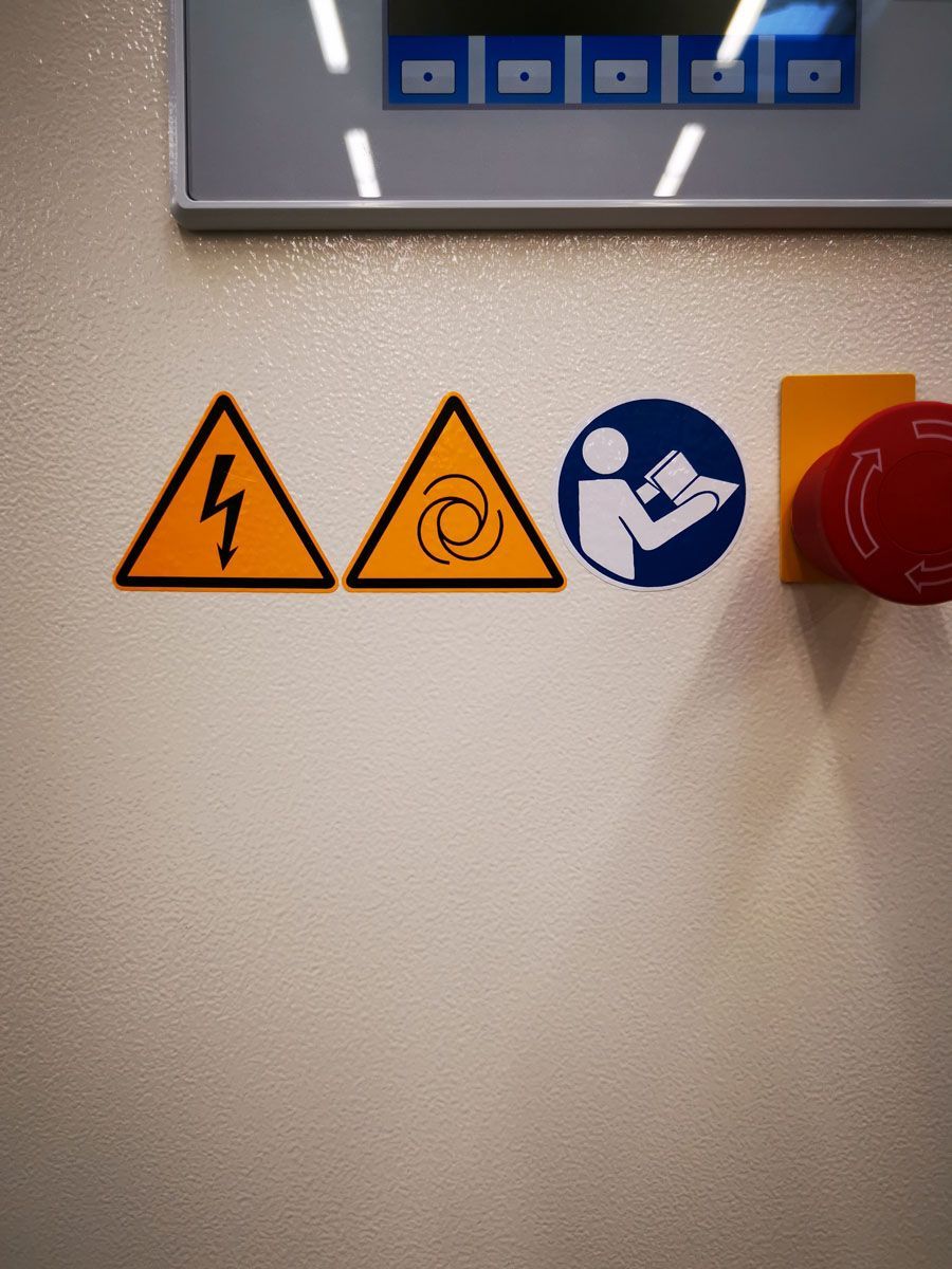 Eine weiße Wand mit Warnschildern und einem roten Knopf