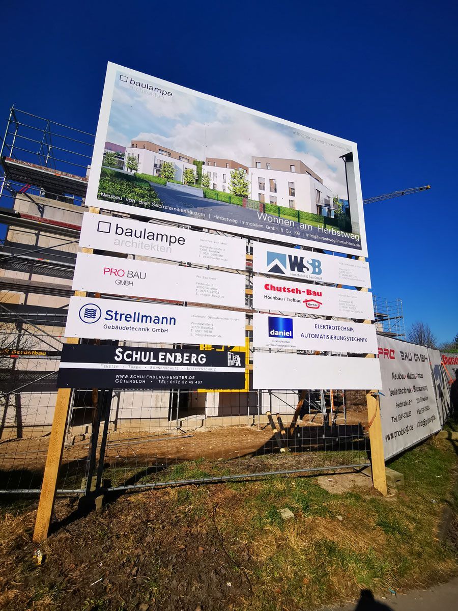 Vor einem im Bau befindlichen Gebäude steht eine große Plakatwand.