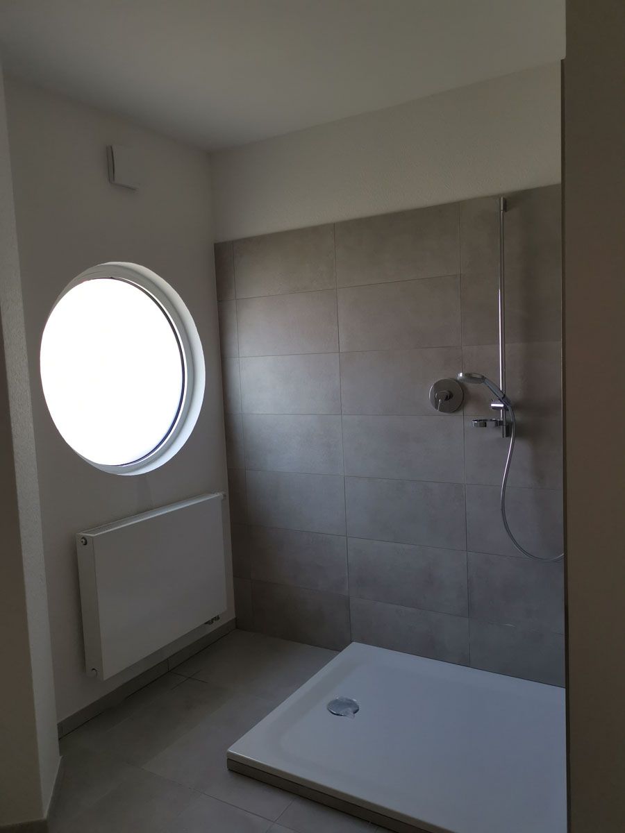 Ein Badezimmer mit Dusche und rundem Fenster.
