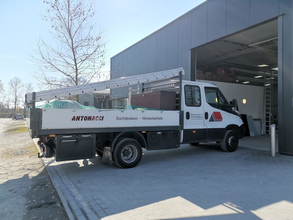 Ein weißer Lastwagen mit einer Leiter auf der Ladefläche steht vor einem Gebäude.
