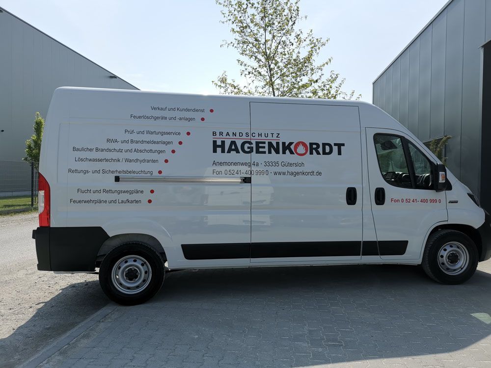 Ein weißer Lieferwagen mit dem Wort Hagenkordt an der Seite steht vor einem Gebäude.