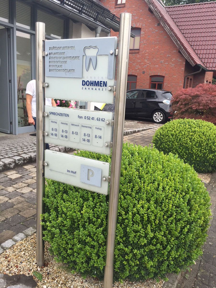 Vor einem Backsteingebäude steht ein Schild einer Zahnarztpraxis.