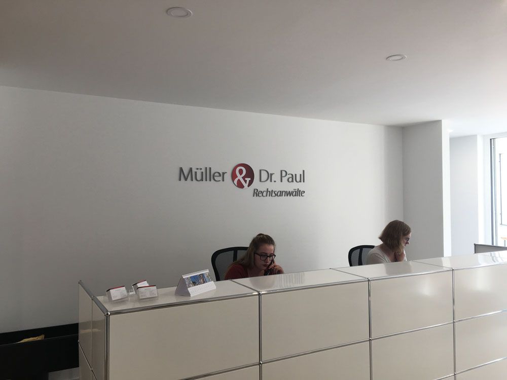 Eine Frau sitzt an einem Schreibtisch im Empfangsbereich und telefoniert mit einem Mobiltelefon.