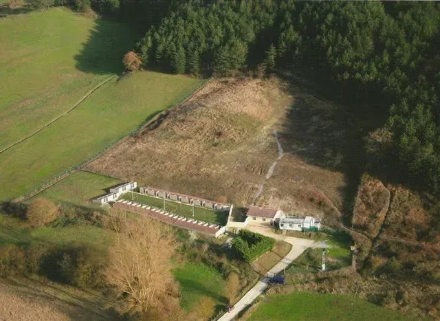 Vista aérea de una granja rural con campos, una gran ladera despejada y un bosque cercano.
