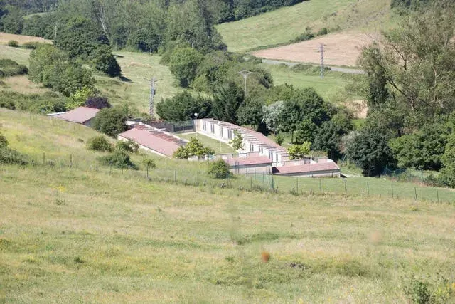 Casa de campo rural en un valle verde, rodeada de colinas cubiertas de hierba y árboles.