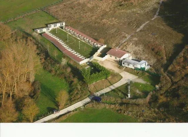 Vista aérea de un complejo de edificios rurales con tejados rojos, rodeado de campos y árboles.