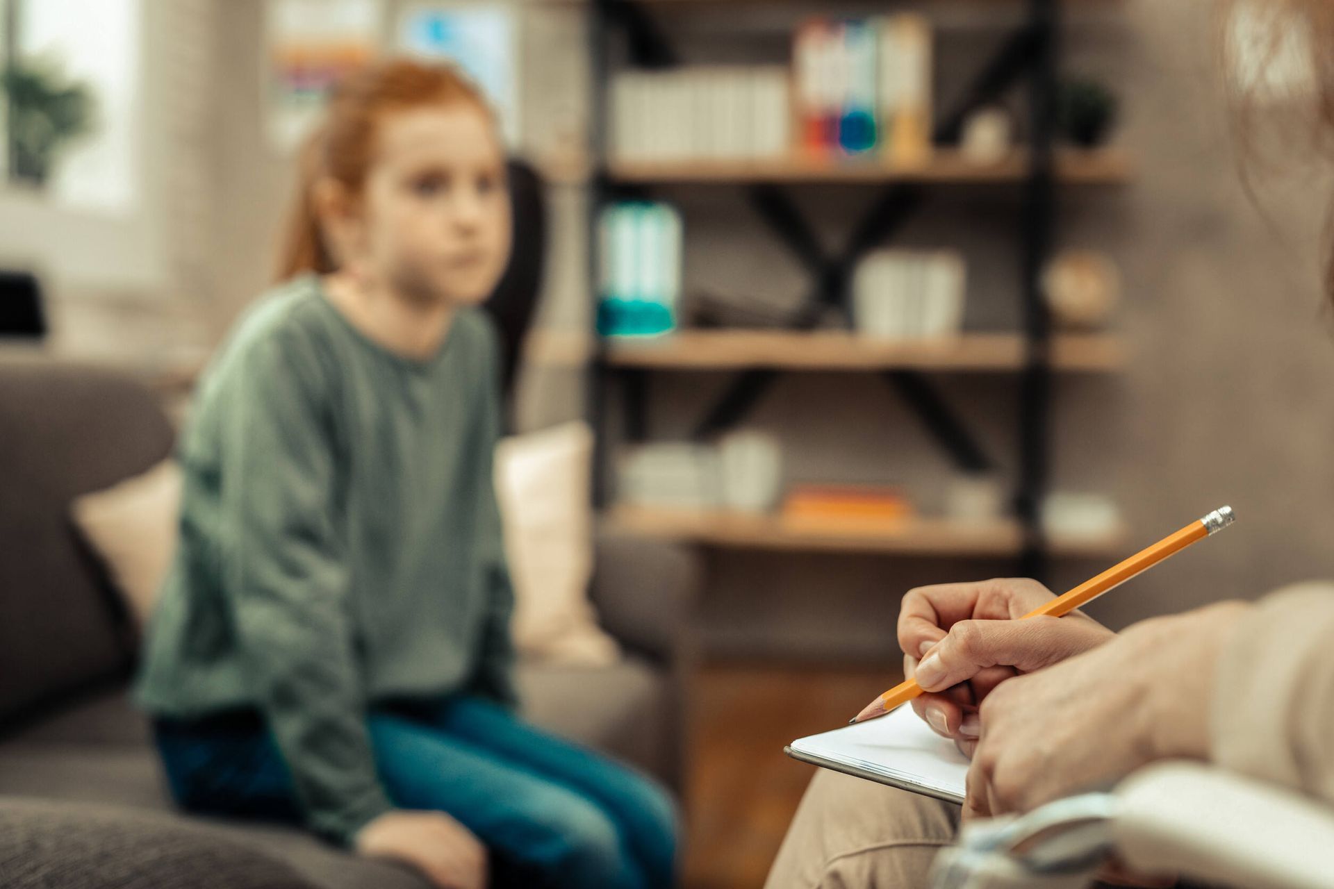 Una mujer está sentada en un sofá hablando con un niño mientras un hombre escribe en un cuaderno.
