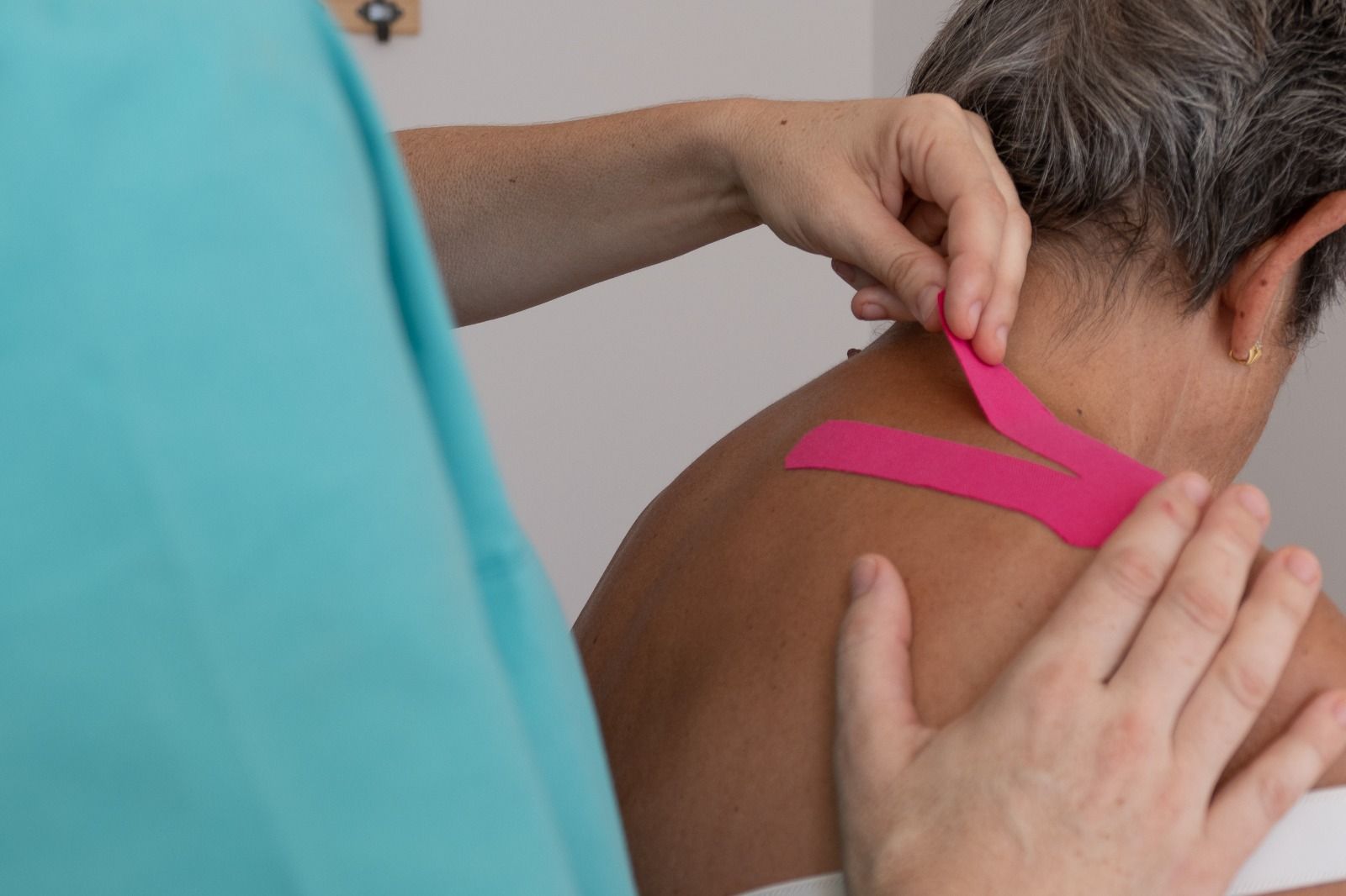 Una persona está colocando cinta kinesiológica rosa en el cuello de una mujer.