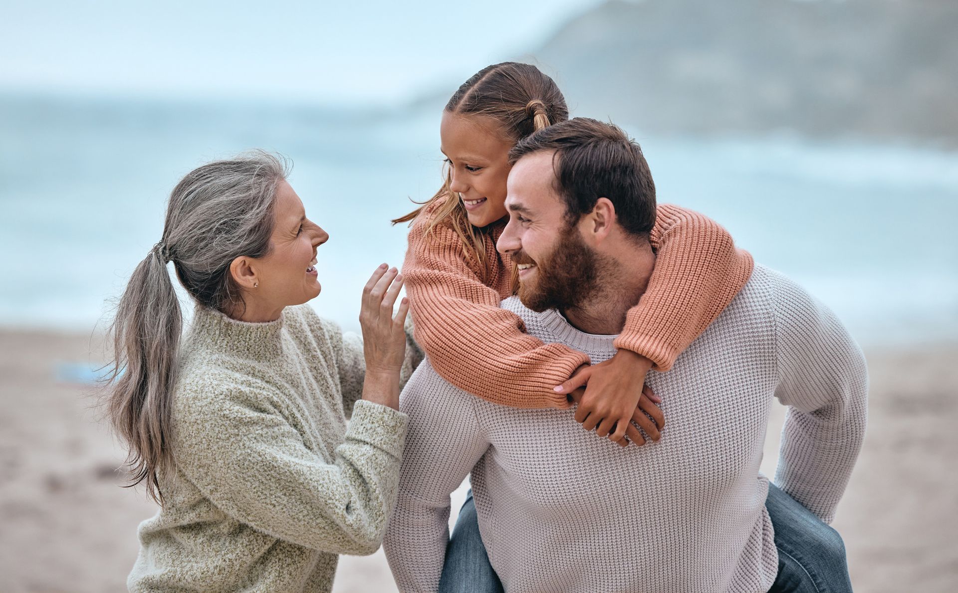 Un hombre lleva a una niña sobre sus hombros en la playa.
