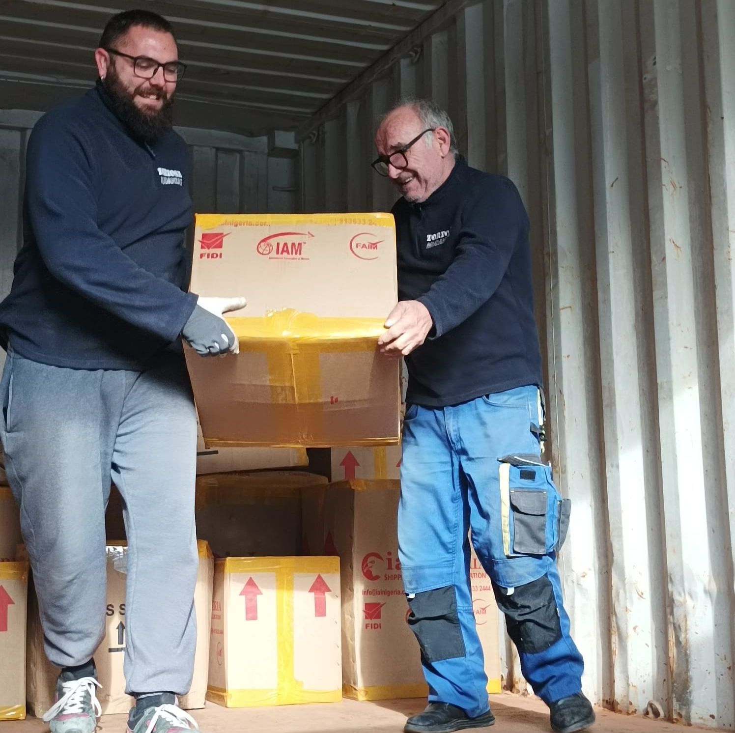 Dos hombres están parados uno al lado del otro sosteniendo una caja de cartón que dice 