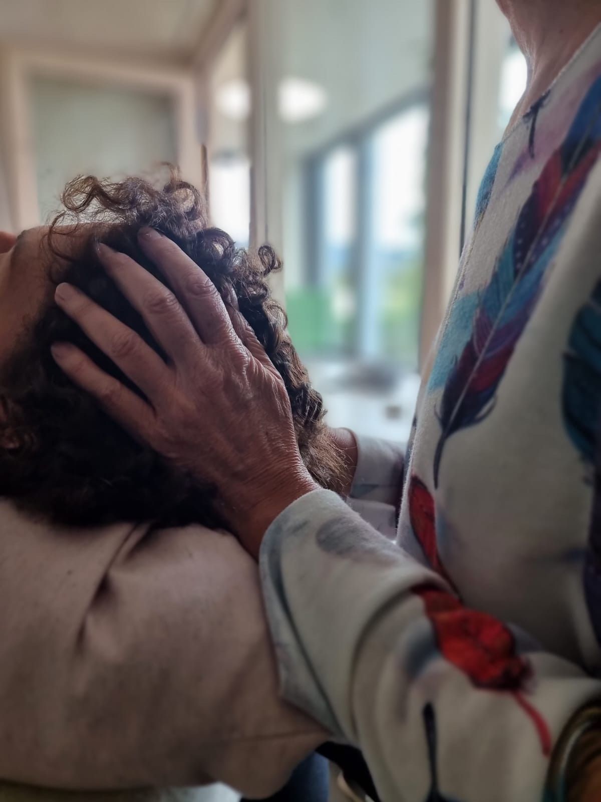 Une personne reçoit un massage de la tête ; une main repose délicatement sur sa tête. On aperçoit une manche à motifs.