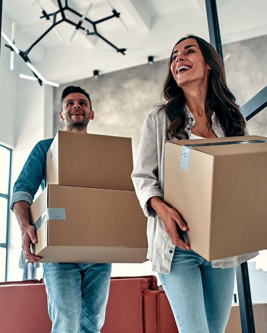 Un couple portant des cartons de déménagement à l'intérieur de leur nouvelle maison.