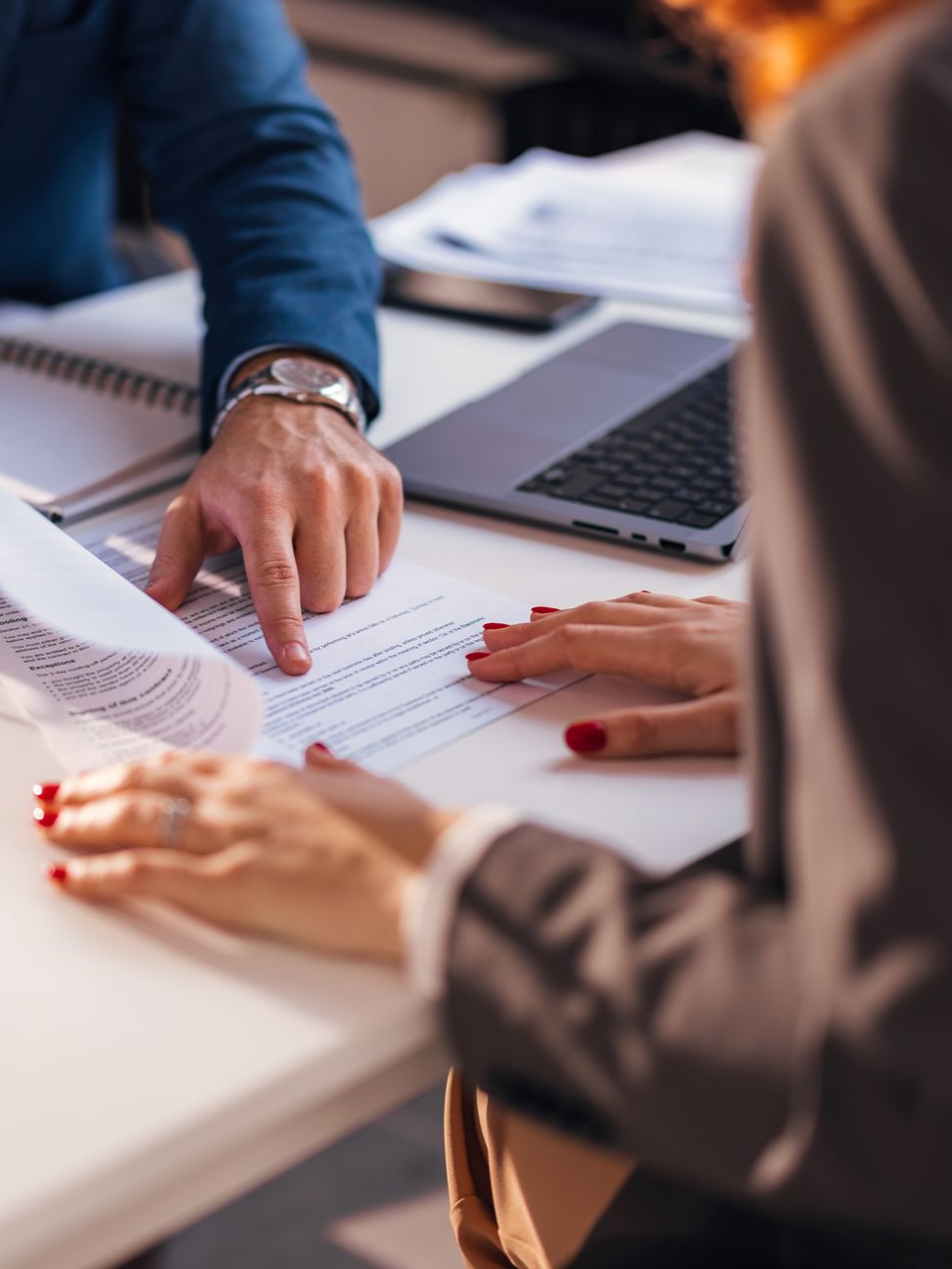 Des mains pointent du doigt des documents posés sur une table, à côté d'un ordinateur portable.