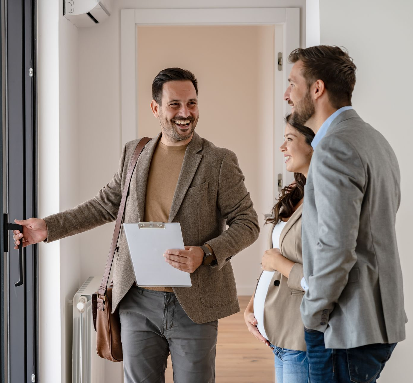 Un agent immobilier ouvre la porte à une femme enceinte et à un homme.