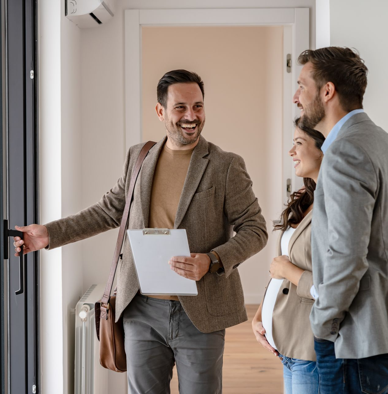 Un agent immobilier souriant ouvre la porte à un couple.
