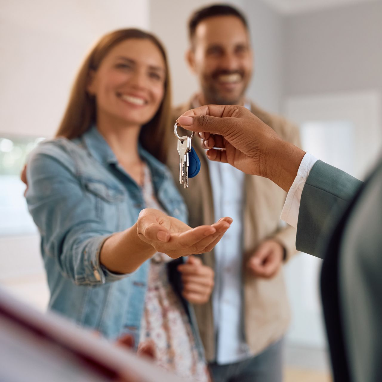 Une personne remet les clés à un couple souriant dans une maison.