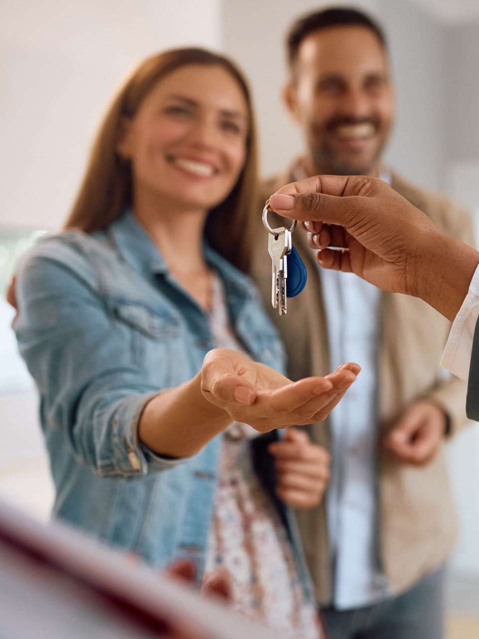 Une personne remet des clés à un couple souriant.