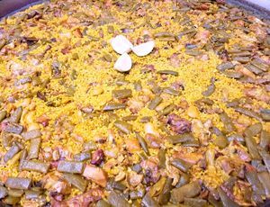 Una olla grande llena de arroz, judías verdes, carne y ajo.