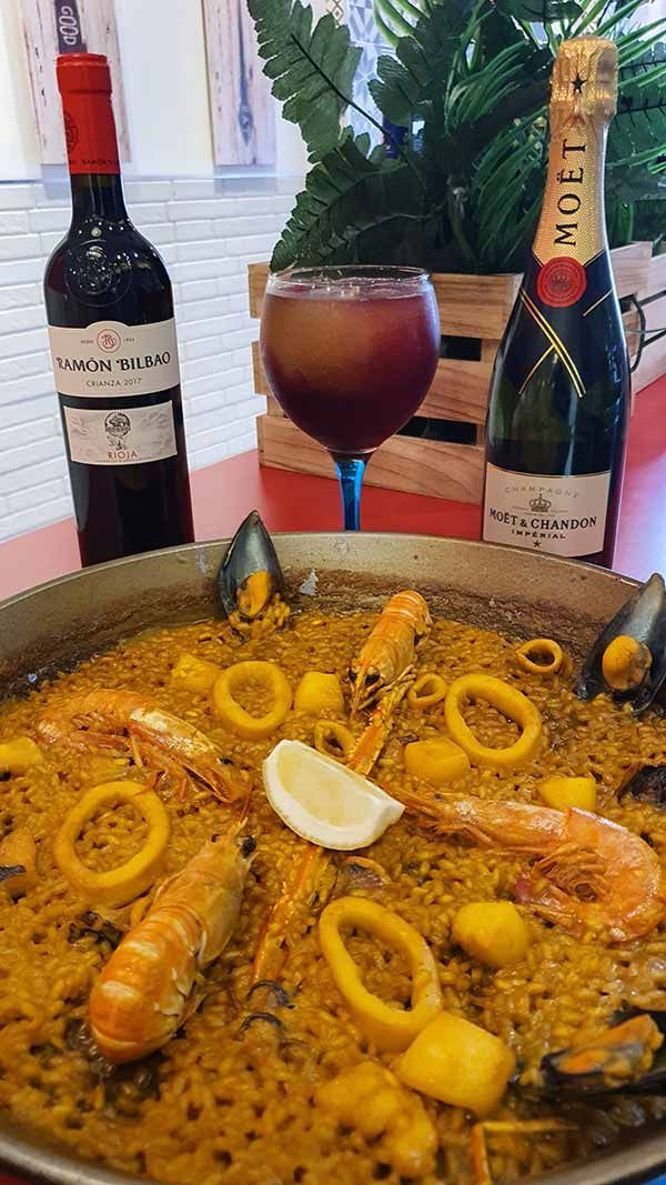 Una paella con marisco y una copa de vino en una mesa.