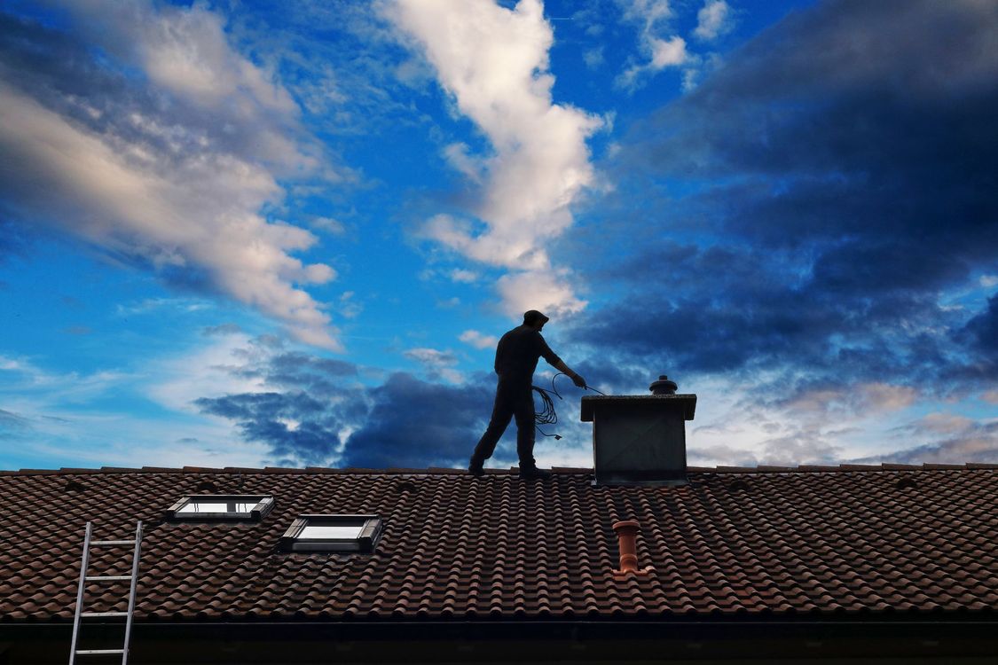 Un homme sur un toit à contre-jour ramonant une cheminée.