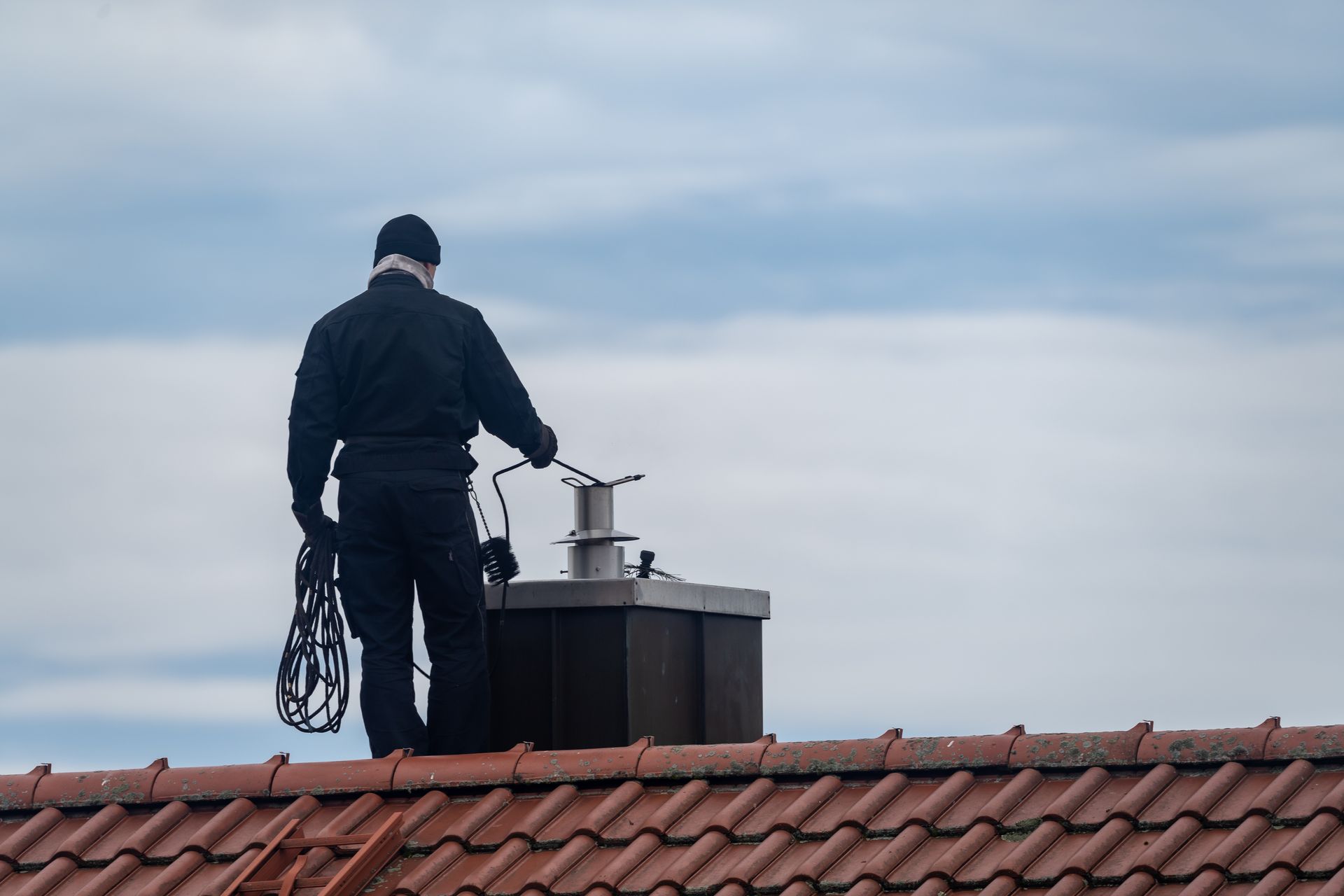 Un homme de dos ramonant une cheminée.
