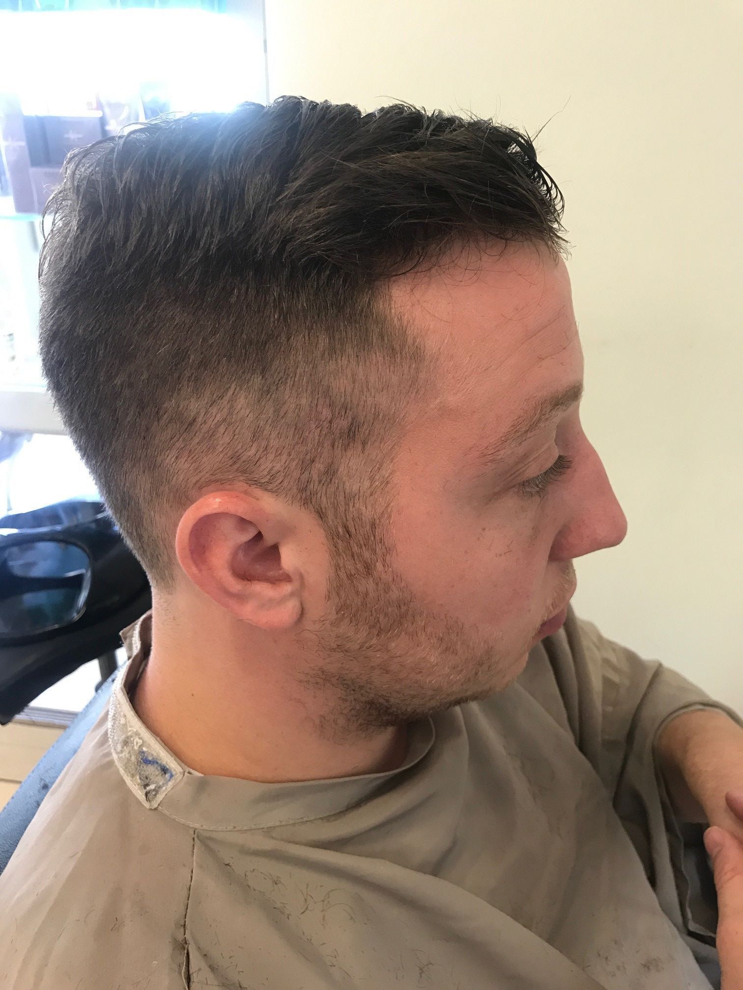 Mann mit kurzem, dunklem Haar, ausgeblichenen Seiten und Spitzbart, in einem Friseurstuhl.